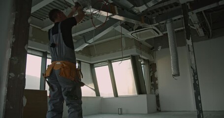An electrician installs wiring in a new office building. He works diligently, ensuring the electrical systems are properly set up.