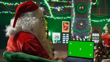 Santa Claus looking at letter received from kids on green screen laptop. Person wearing Santa costume reads wish lists written by children for Christmas on chroma key notebook, camera A