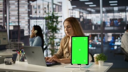 General manager reviewing a document with reports and isolated mockup, evaluating performance metrics to ensure company productivity. Uses her laptop to make informed decisions. Camera B.