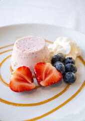 Panna Cotta Served on a White Plate Decorated with Blue Berries, Strawberries and Light Cream