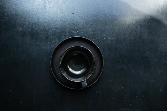 an empty black cup stands on a saucer with crumbs on a black windowsill
