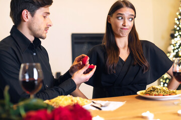Proposal Failure. Man giving open box with engagement ring, confused young woman in doubt looking...