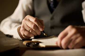 Caucasian middle aged man writing with fountain pen on notepad, close up of hands showing gold wedding ring and formal attire, capturing detail of professional or personal work