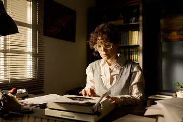Caucasian young adult woman typing on typewriter at desk in office setting, wearing glasses and...