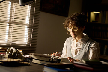 Caucasian young adult woman sitting at desk typing on vintage typewriter, wearing glasses, focused...