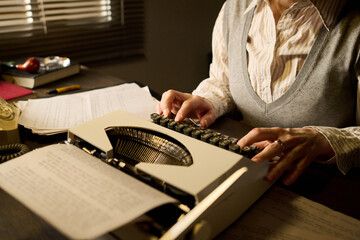 Middle aged Caucasian woman typing on vintage typewriter at desk, working with documents and papers...