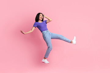 Full length of charming glad carefree delightful asian woman millennial having fun and good mood, jumping at studio and looking away isolated over colorful pink background with copy space