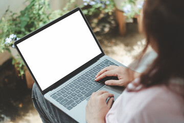 Young female freelancer or student typing on a laptop with a blank white screen while sitting relaxed outdoors. Mockup design for online business, remote work, education, digital marketing, lifestyle.
