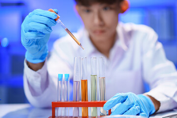 Scientists working in Laboratory using pipette dropping liquid sample into test tube.