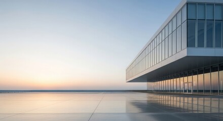 Modern architectural building with glass facade reflecting the soft colors of a serene sunset over a calm body of water
