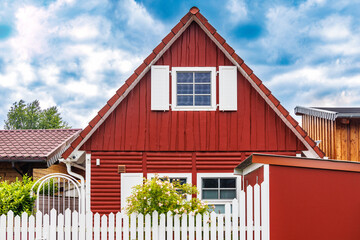 Red wooden residential house with white picket fence under cloudy sky