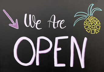 We are open sign with a downward arrow and pineapple drawing on blackboard