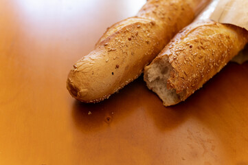 Two French baguettes on wooden table. Fresh pastries in pastry shop. Baking bread. French cuisine in restaurant menu. Lunch time. Paper packaging for bread.