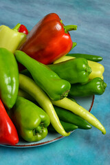 Plate with different fresh peppers on blue background