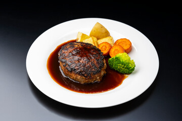 黒背景にデミグラスソースのハンバーグと彩り野菜