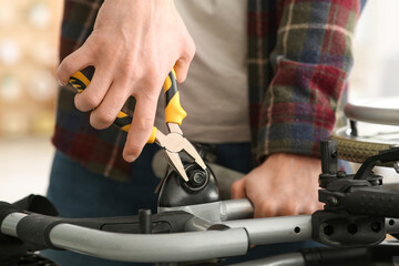 Young man with pliers repairing wheelchair at home, closeup