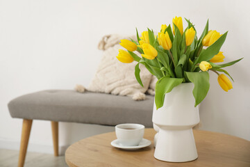 Cozy bench with cushions and vase of yellow tulips on coffee table in living room