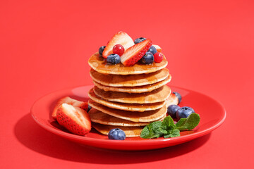 Plate with tasty pancakes, strawberry and blueberries on red background