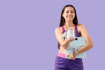Sporty young woman with chia seed pudding and weight scales on lilac background