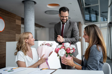Businesswomen receiving flowers from manager in modern office
