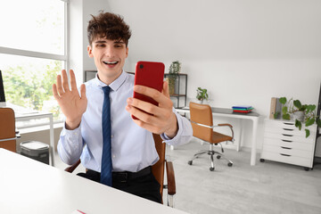 Young businessman video chatting with mobile phone at table in office