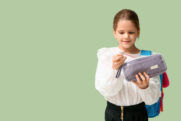 Cute little happy girl with backpack, pen and pencil case on green background