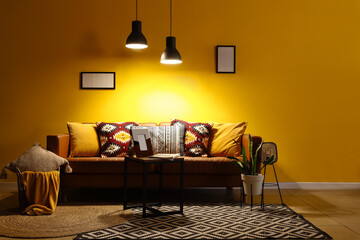 Interior of living room with sofa, table and glowing lamps at night