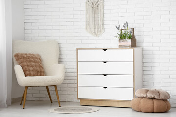 Basket with beautiful Muscari flowers on chest of drawers, poufs and stylish armchair near light brick wall