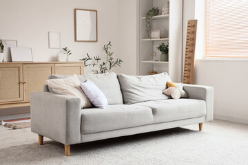 Interior of modern living room with sofa, shelving unit, commode and wooden stadiometer near window