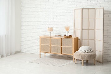 Interior of modern room with folding screen, pouf and chest of drawers