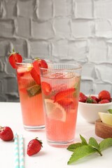 Refreshing drink with strawberries, mint, lemon and ice on white table against grey textured background, closeup