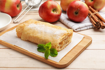 Tasty apple strudel with powdered sugar, mint, fruits and cinnamon on wooden table, closeup