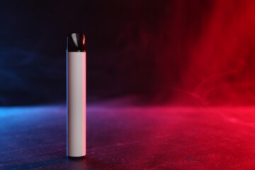 Electronic smoking device on black table in red light. Space for text