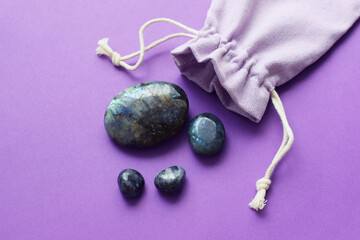 Beautiful natural labradorite semi-precious stones and fabric bag on purple background. Healing...