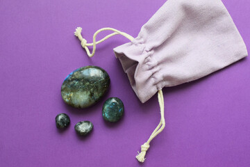Beautiful natural labradorite semi-precious stones and fabric bag on purple background. Healing...