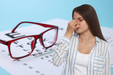 Woman with eyesight problems, glasses and vision test chart on light blue background