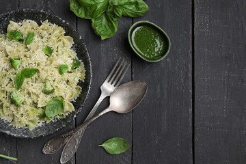 Bowl of delicious farfalle pasta with broccoli and basil leaves on black wooden background