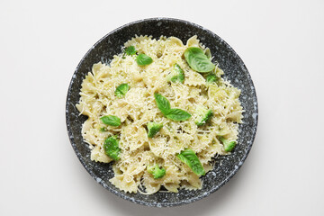 Bowl of delicious farfalle pasta with broccoli and basil leaves on grey background