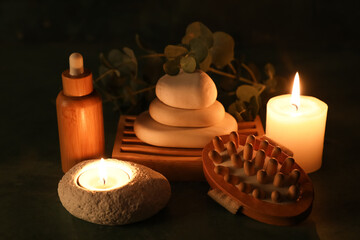 Composition with spa stones, burning candles and bottle of cosmetic product on black background, closeup