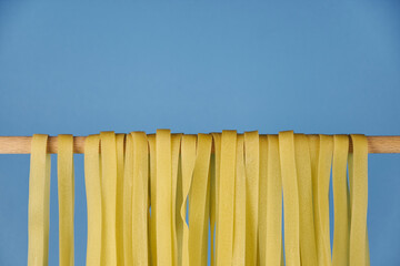 Fresh egg fettuccine noodles, drying in the foreground against a light blue background with copy space
