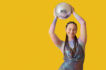 Fashionable young woman with dreadlocks and disco ball on yellow background
