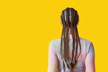 Fashionable young woman with dreadlocks on yellow background, back view