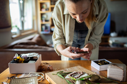 Woman photographing handmade jewelry products for online shop at home