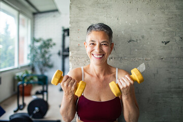 Smiling senior woman lifting dumbbells at gym