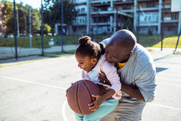 Grandfather teaching granddaughter how to play basketball outdoors