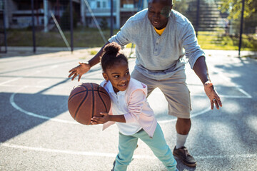 Grandfather teaching granddaughter how to play basketball outdoors