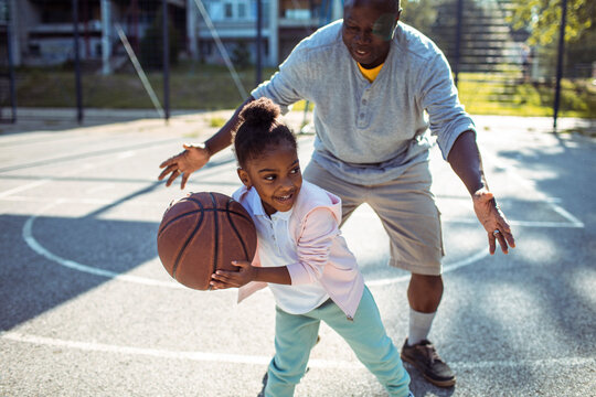 Grandfather teaching granddaughter how to play basketball outdoors - Powered by Adobe
