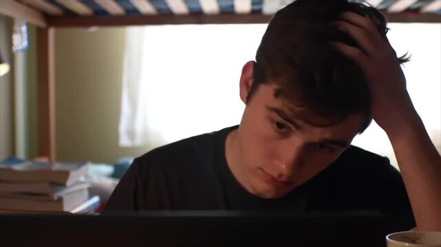 Dedicated student studying late at night in his dorm room with a laptop.