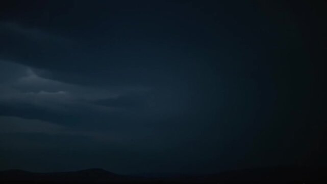 Lightning Strike over Hills at Night. Dark storm clouds moving ominously. Dramatic weather for use in backgrounds