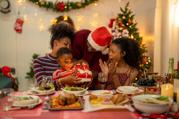An African American family gathers for a festive Christmas party, enjoying snacks, drinks, and laughter in their decorated living room. Concept for holiday entertaining and joyful feasts.